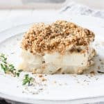 A piece of creamy cauliflower casserole on a white plate with a sprig of thyme.