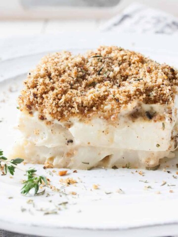 A piece of creamy cauliflower casserole on a white plate with a sprig of thyme.