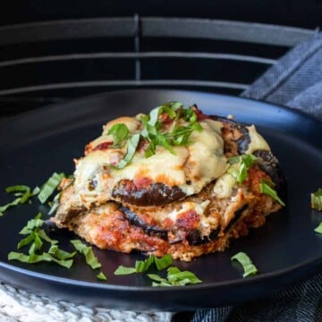 Black plate with a piece of eggplant parmesan topped with sliced basil