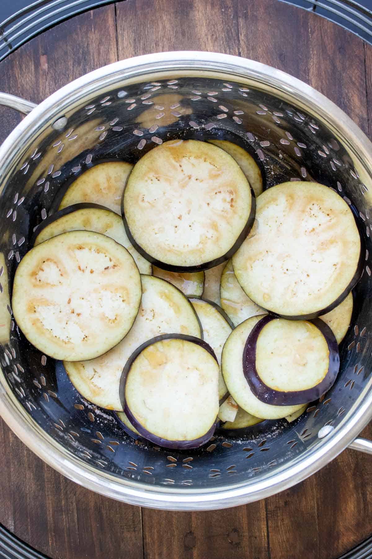 Sliced eggplant in a colander with droplets of water on the surface