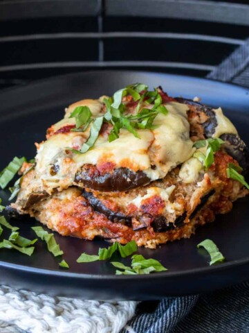 Black plate with a slice of baked eggplant parmesan on it