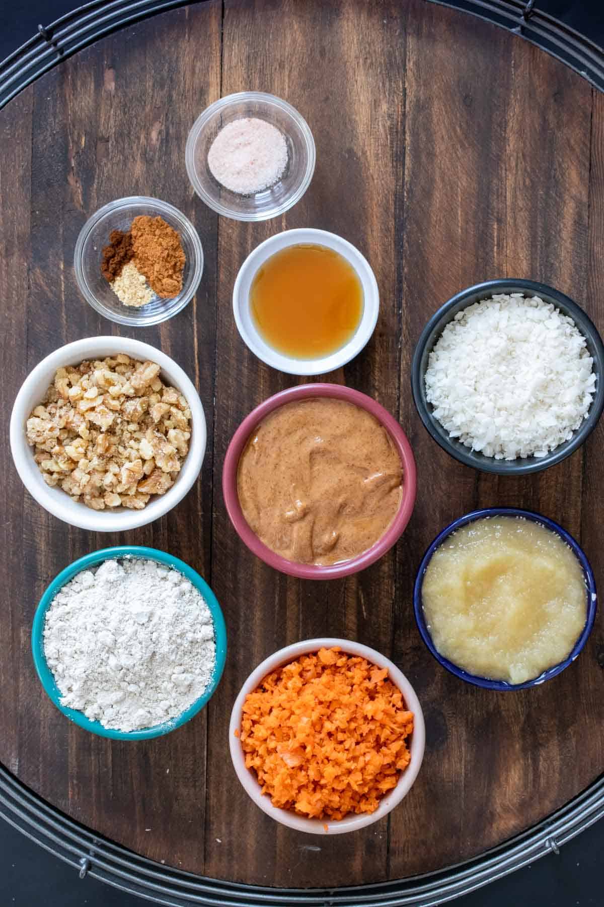 Different colored bowls filled with ingredients to make carrot cake energy balls