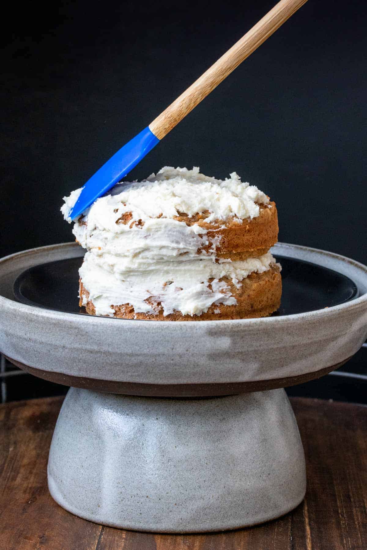 A spatula putting white frosting on a two layer cake