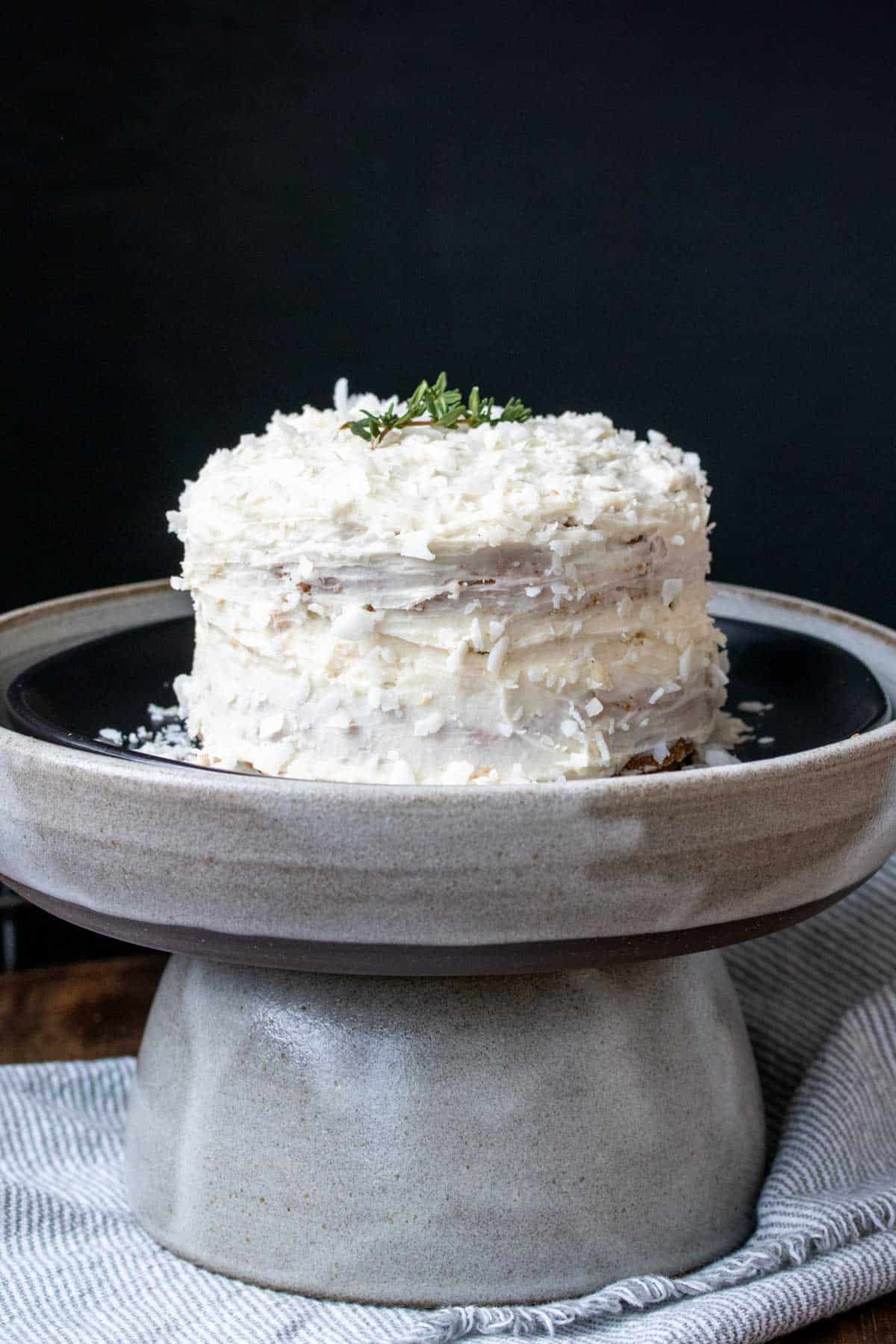 A two layer cake with white frosting on a black plate inside a grey plate