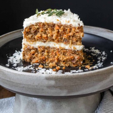 A slice of carrot cake with white frosting on a black plate