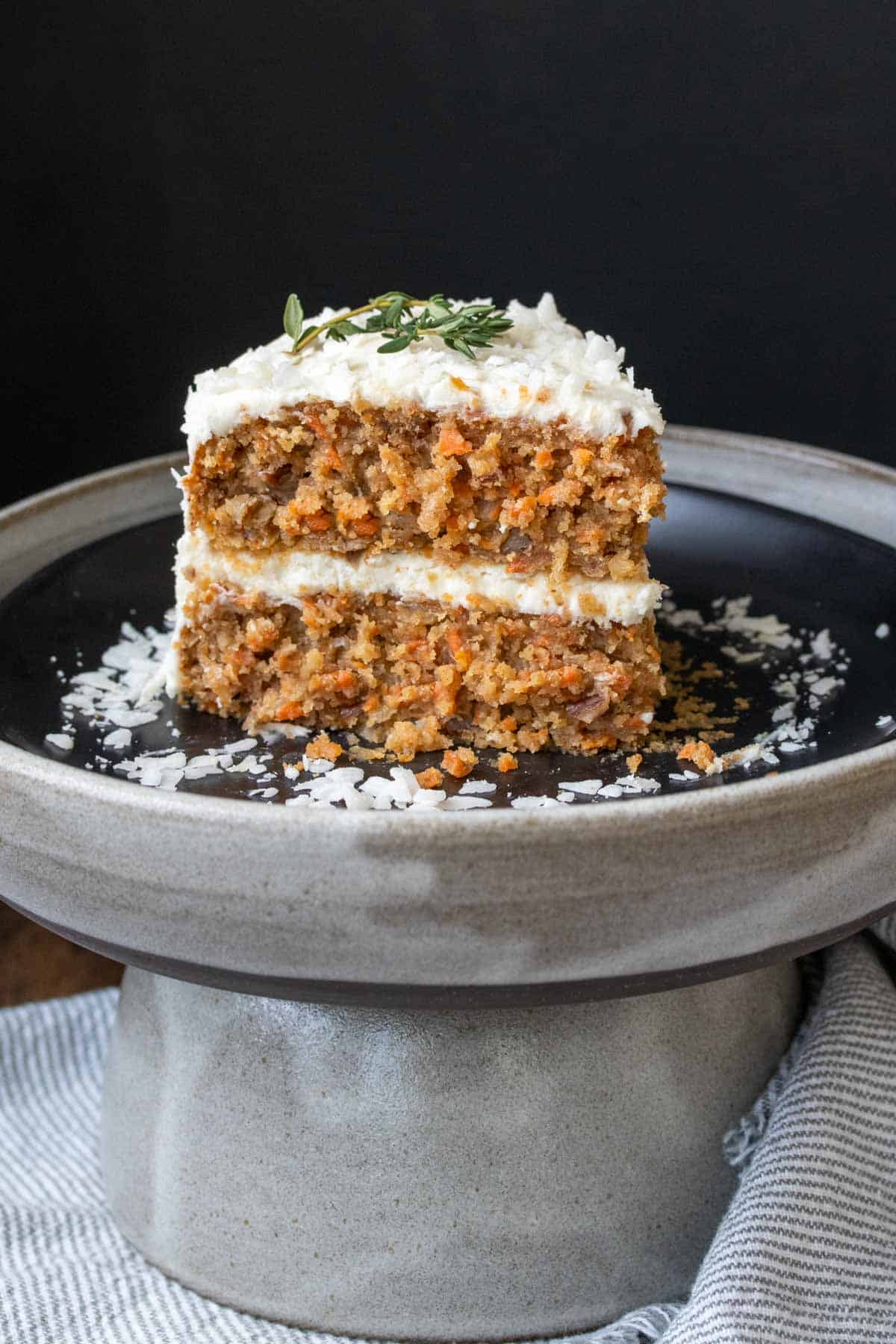 A slice of carrot cake with white frosting on a black plate