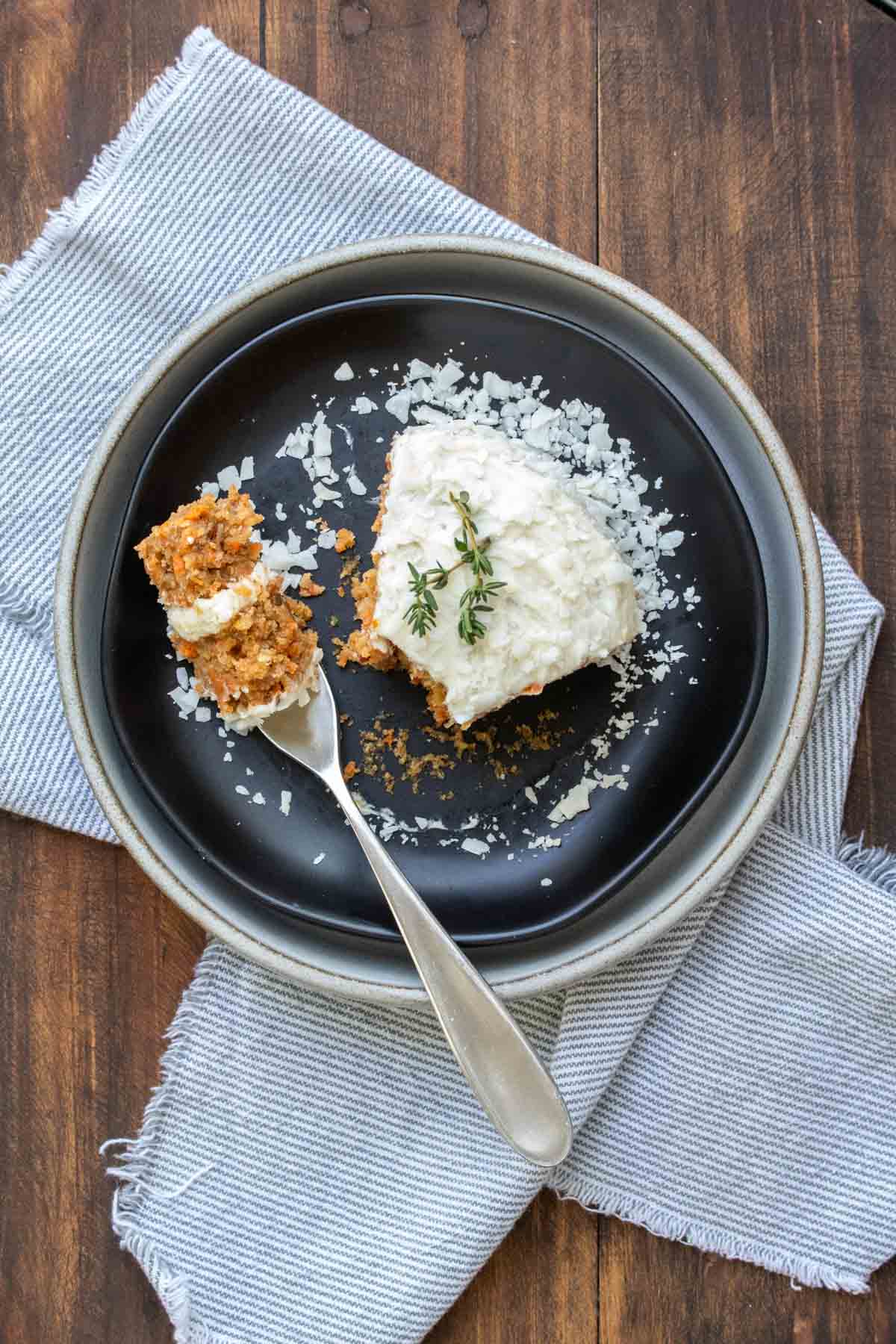Top view of a fork with a bite of carrot cake on it on a black plate