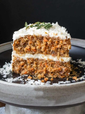 A frosted piece of carrot cake on a black plate with shredded coconut on it.
