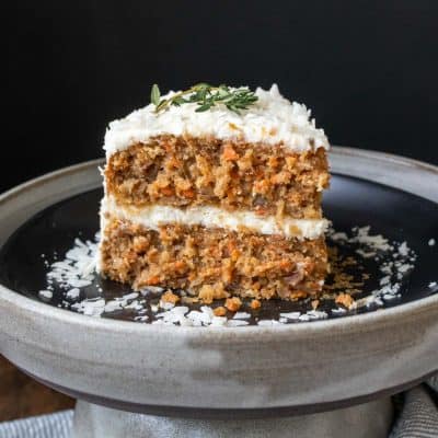 A frosted piece of carrot cake on a black plate with shredded coconut on it