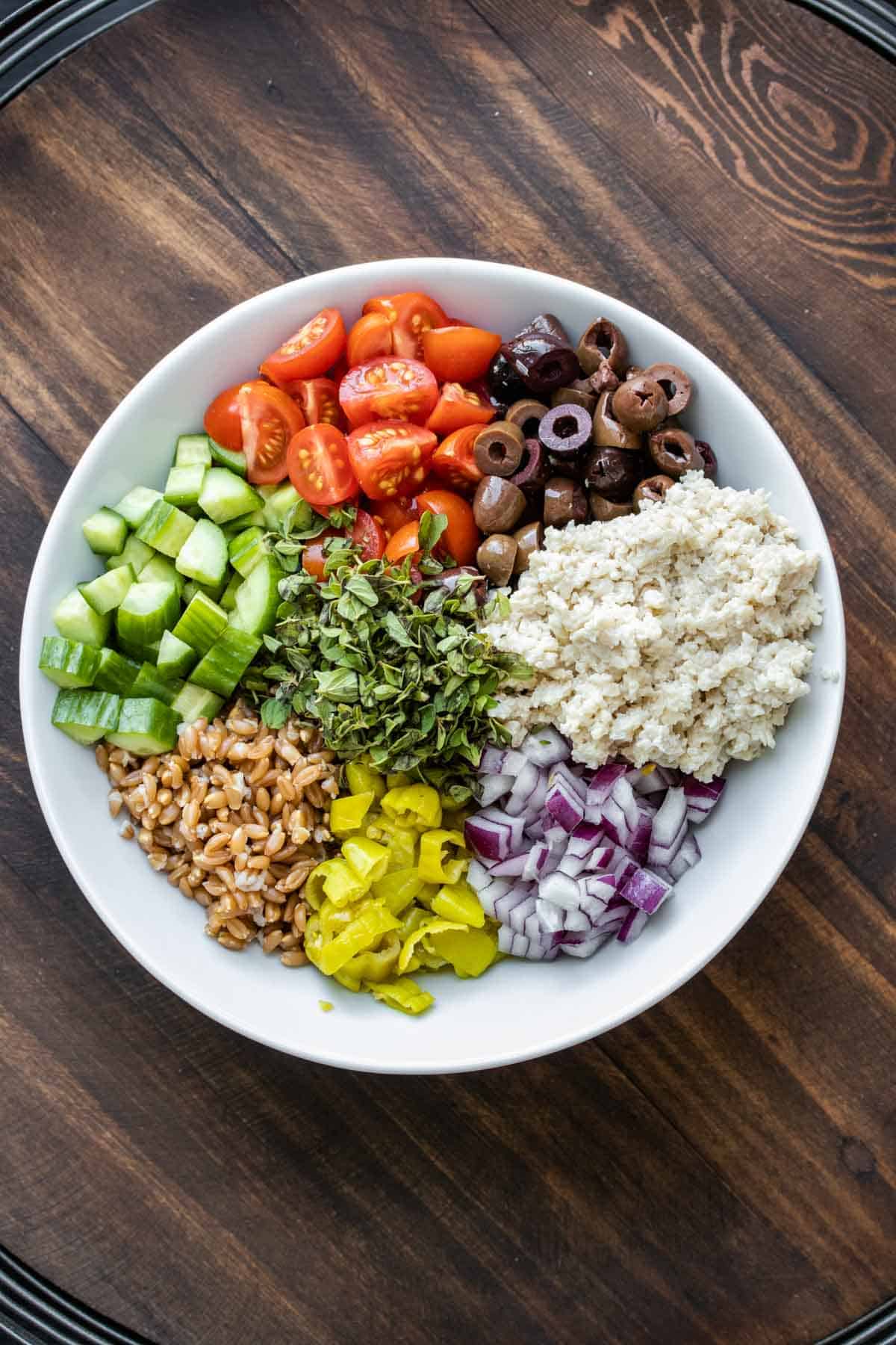 White bowl with farro, veggies and vegan feta in piles.