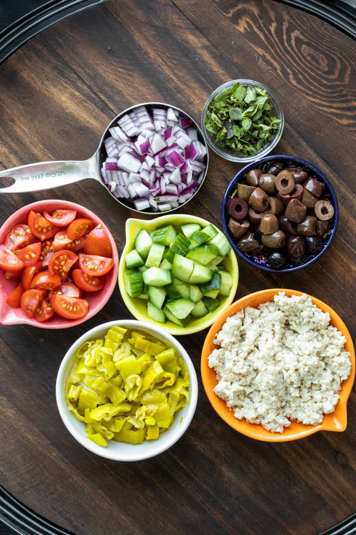 Different ingredients like veggies and vegan feta in bowls on a wooden table.