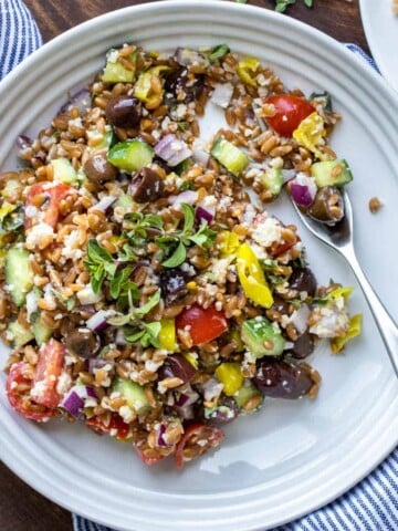 A white plate with a farro based salad in it and oregano sprinkled on top.