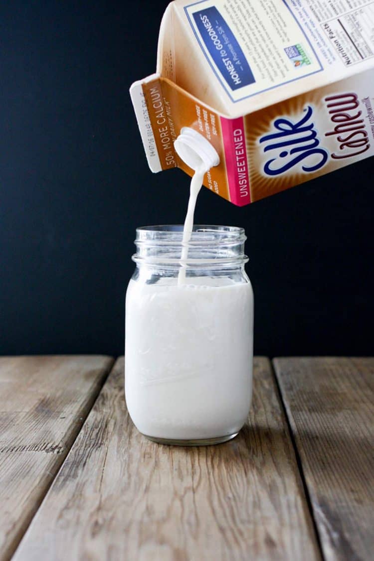 Carton of cashew milk pouring milk into a glass jar