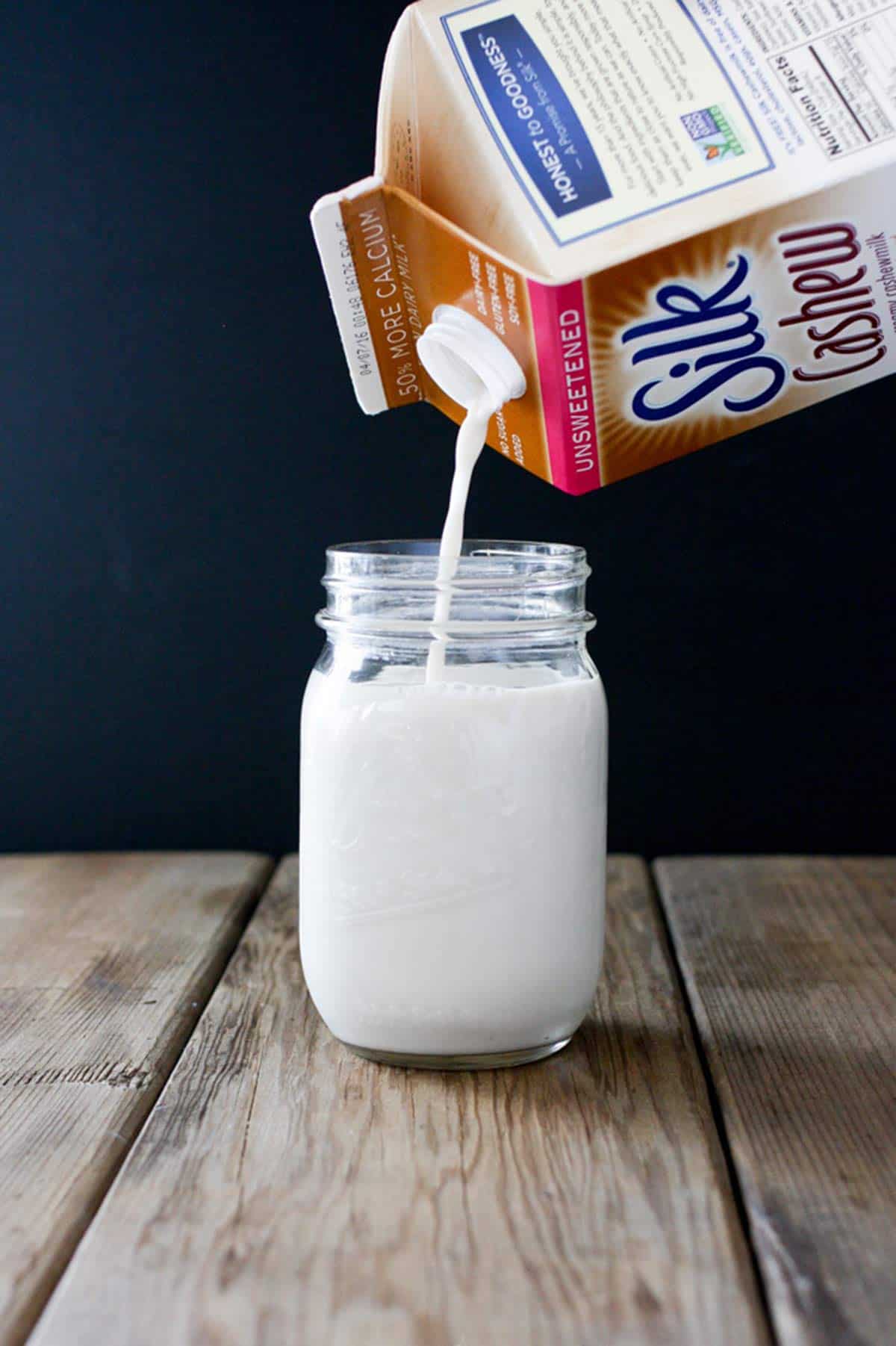 Carton of cashew milk pouring milk into a glass jar.