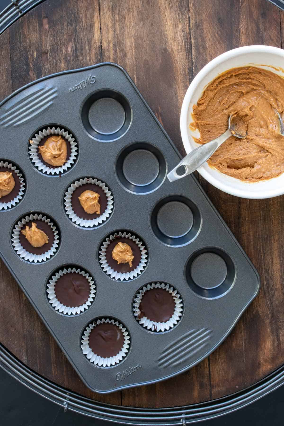 Mini muffin tin with liners filled with melted chocolate and peanut butter