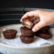 Hand taking a bitten peanut butter cup off of a pile on a plate