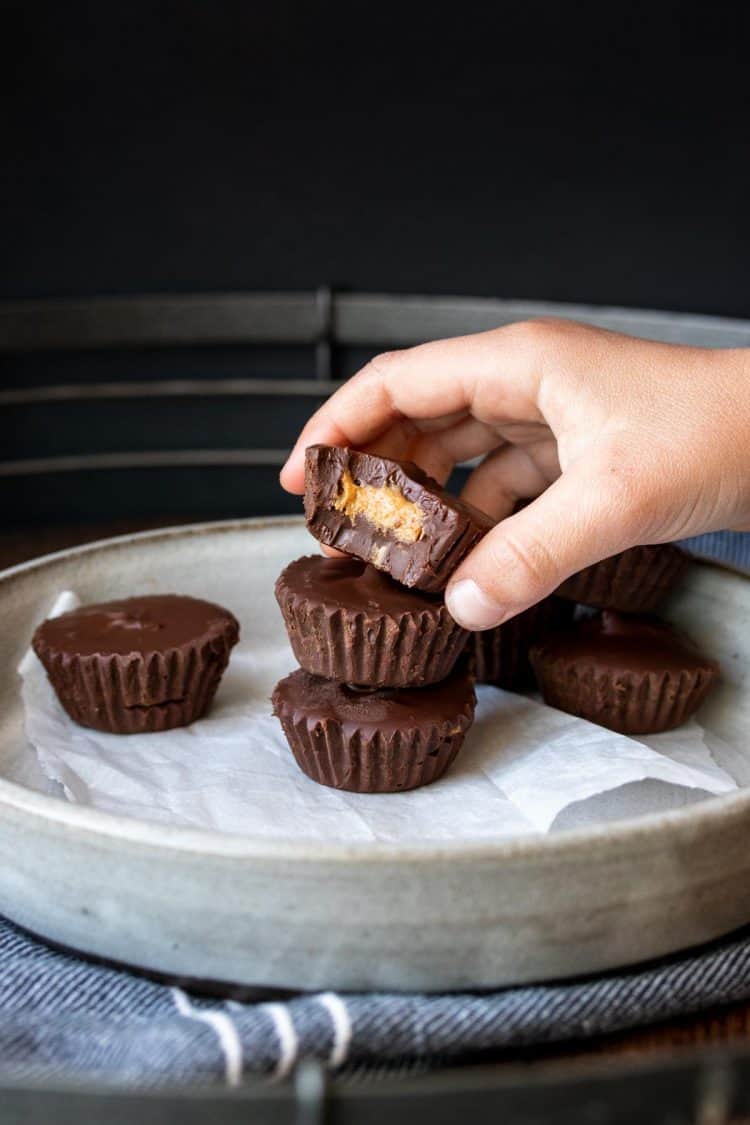 Hand taking a bitten peanut butter cup off of a pile on a plate