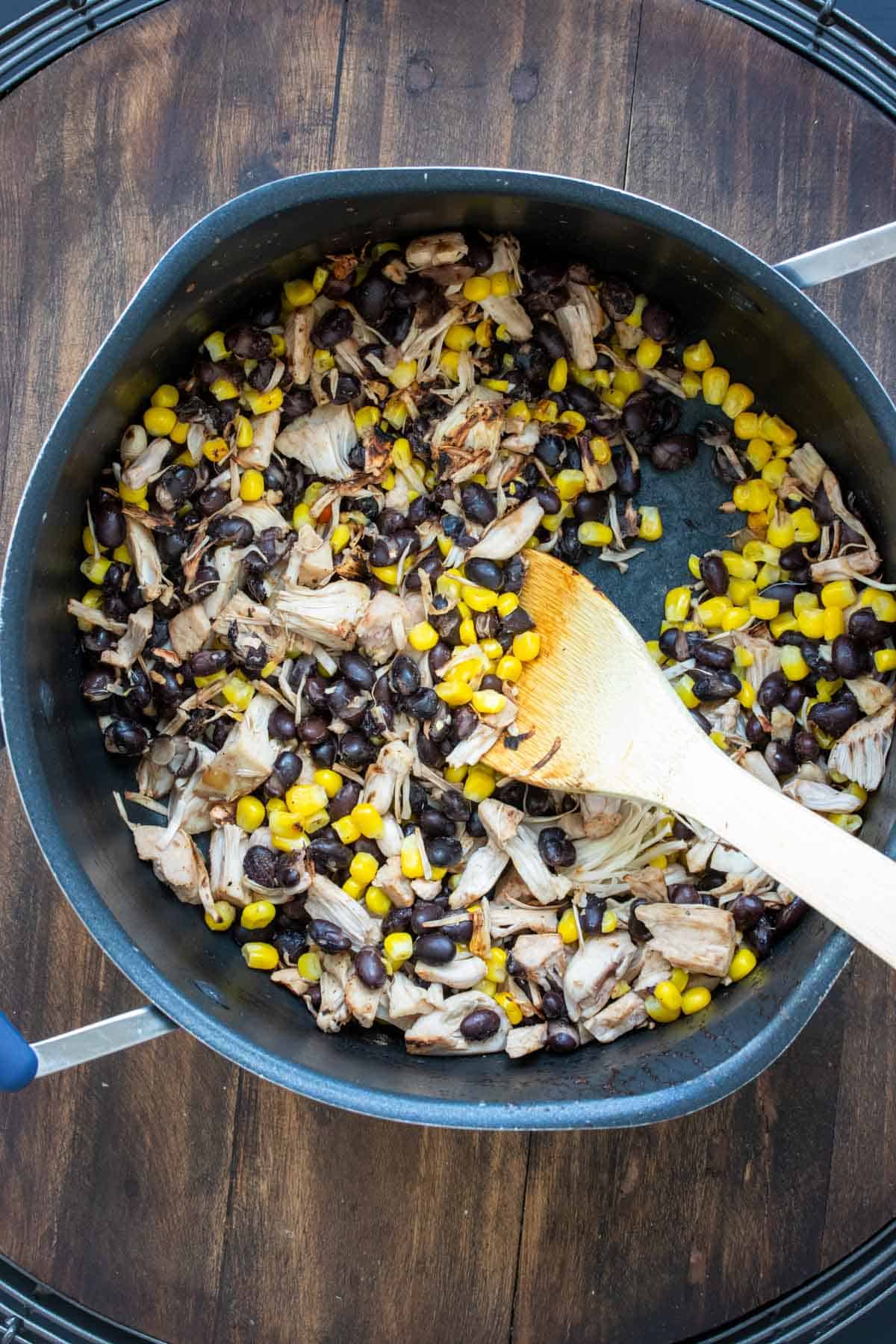 Wooden spoon mixing corn, beans and jackfruit in a pot