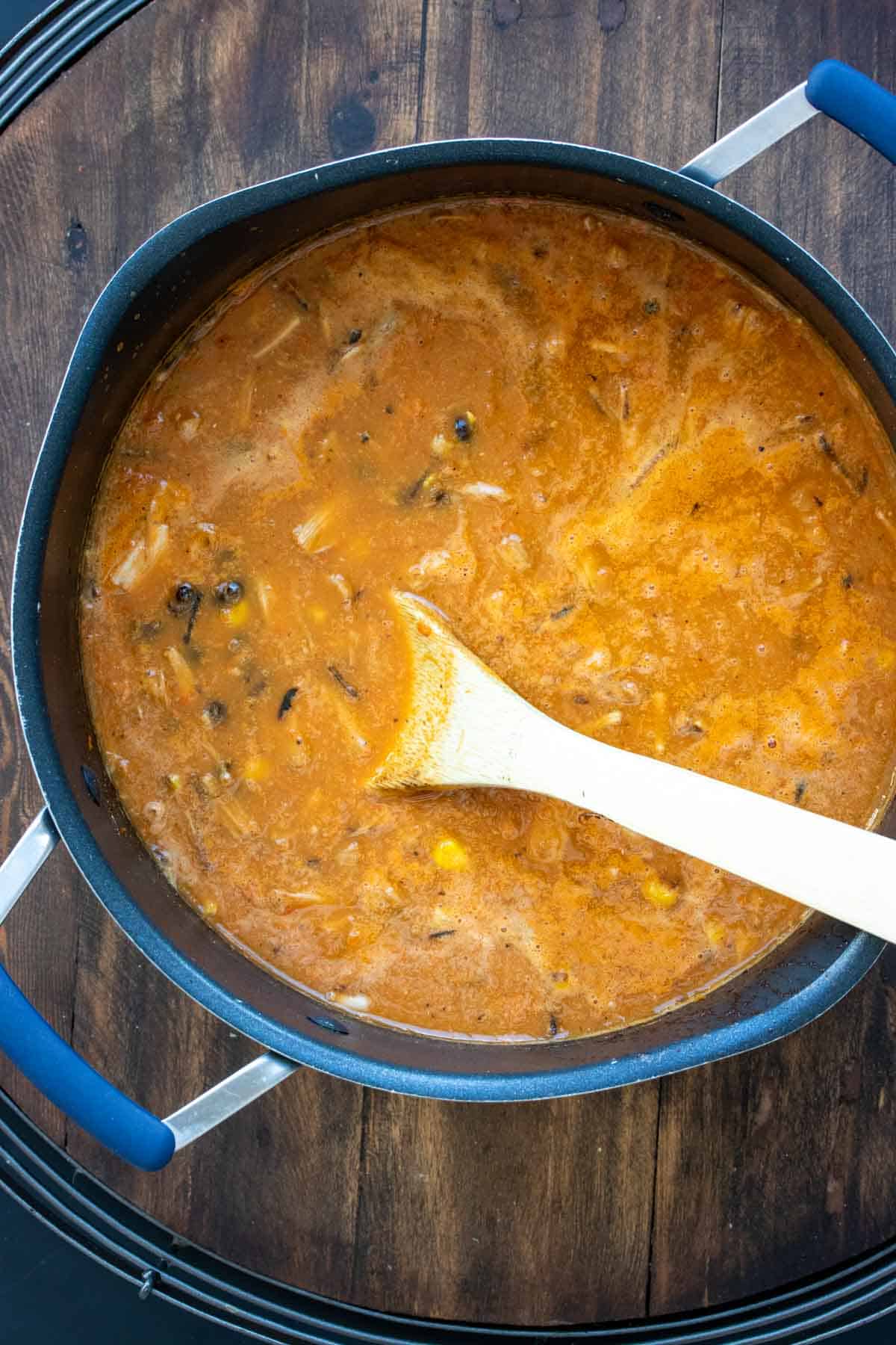 Pot with a red soup being mixed by a wooden spoon