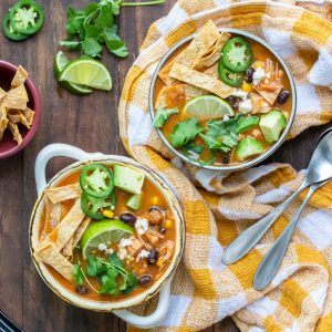 Yellow checked napkin on a wooden surface with bowls of tortilla soup.