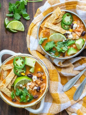 Yellow checked napkin on a wooden surface with bowls of tortilla soup.