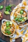 Two soup bowls on a yellow checkered towel that have a jackfruit tortilla soup inside loaded with toppings.