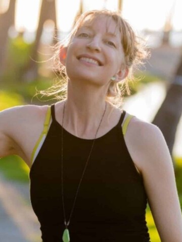 A smiling woman in a black tank top and necklace with green stone hanging