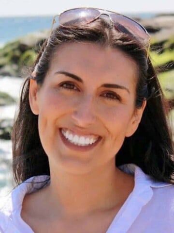 A woman with brown hair and glasses on top of her head smiling