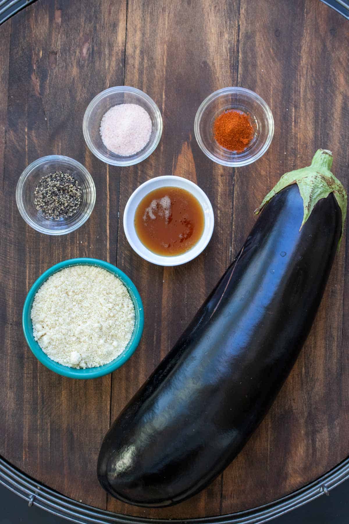 A whole eggplant next to flour and spices on a wooden surface