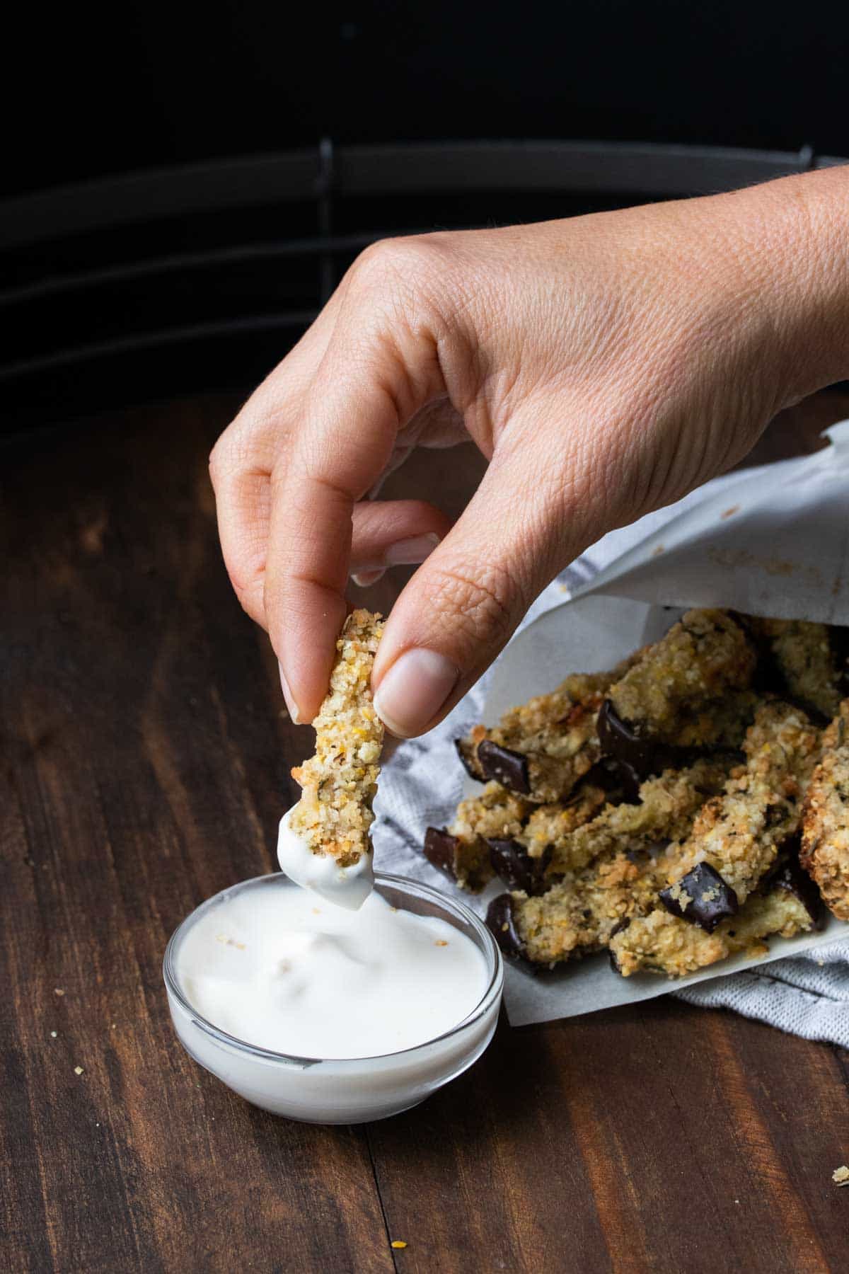 Hand dipping an eggplant fry into a white sauce