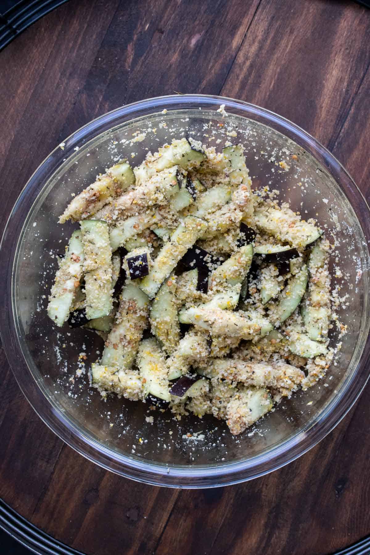 Eggplant sticks covered in crispy topping in a glass bowl.