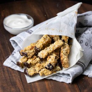 A pile of eggplant fries in parchment paper laying on a wooden surface.