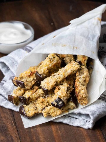 A pile of eggplant fries in parchment paper laying on a wooden surface.