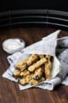 A group of eggplant fries piled into a cone of parchment sitting on a grey towel.