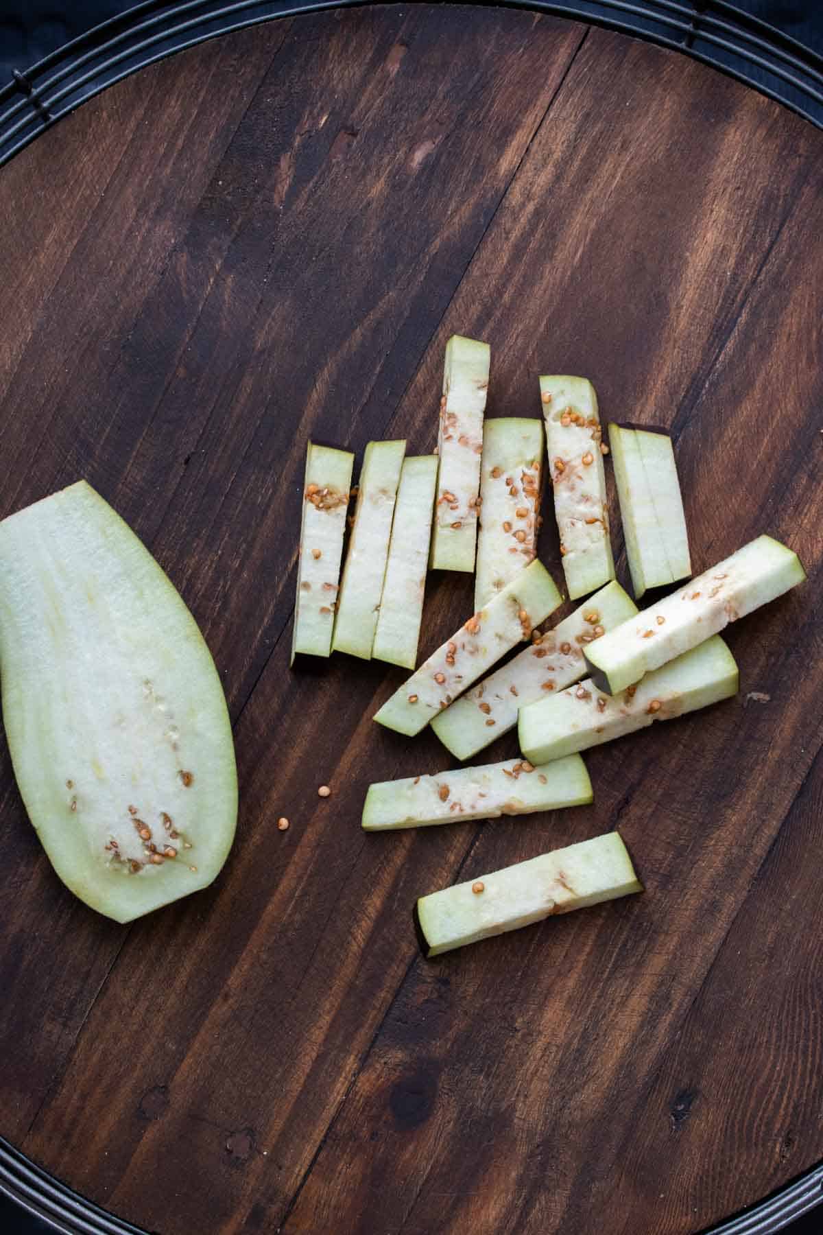 An eggplant cut in half next to a pile of some cut in sticks.