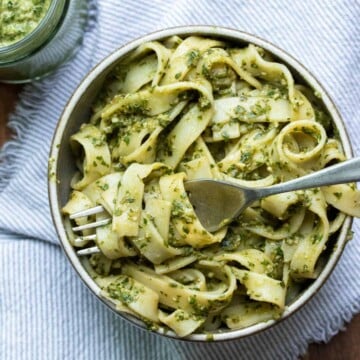 Fork getting a bite of pesto covered fettuccini pasta from a grey bowl