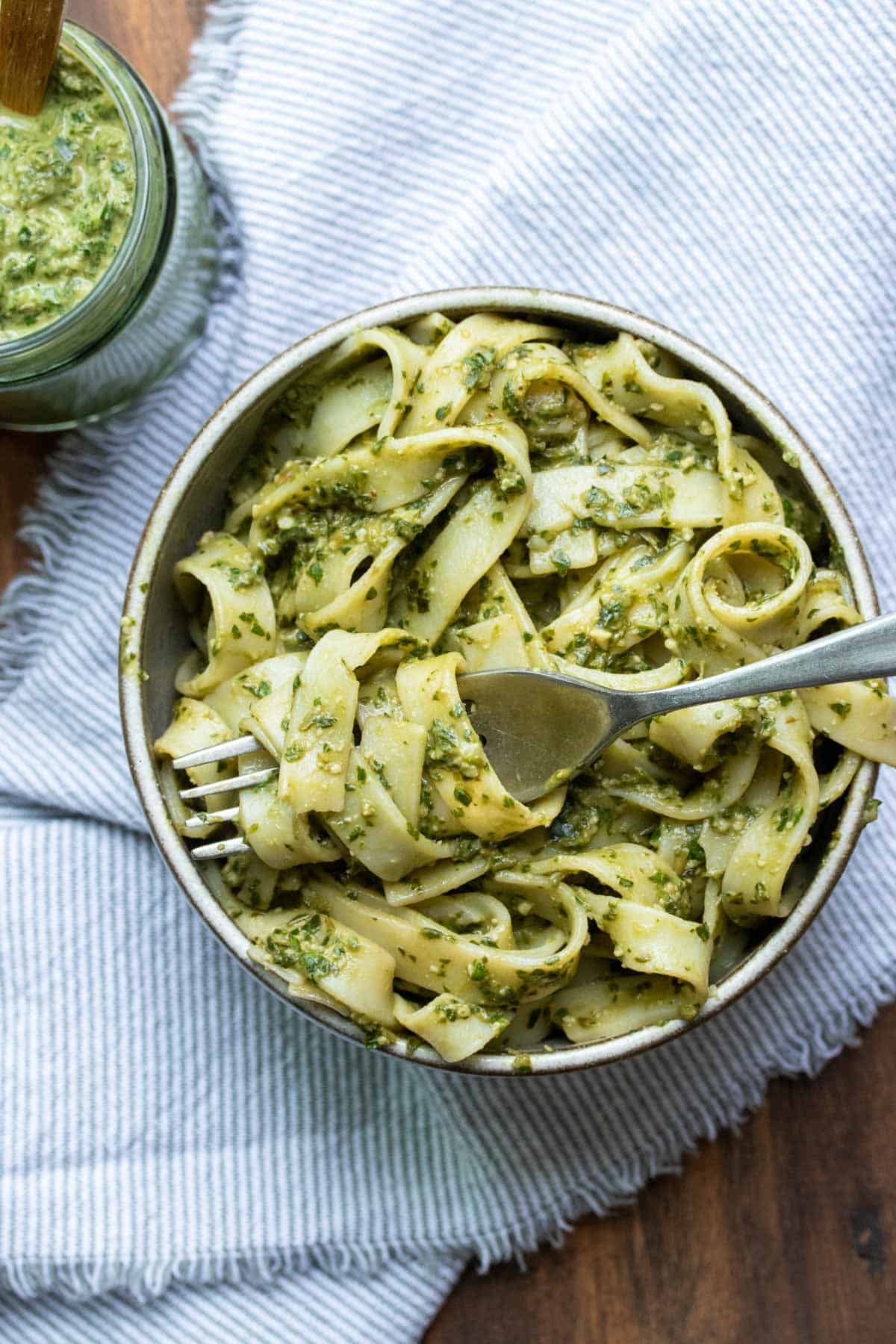 Fork getting a bite of pesto covered fettuccini pasta from a grey bowl