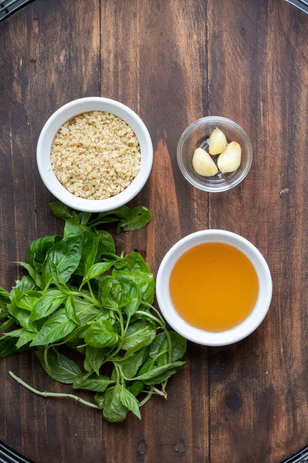 A wooden surface with basil, parmesan, broth and garlic cloves on it