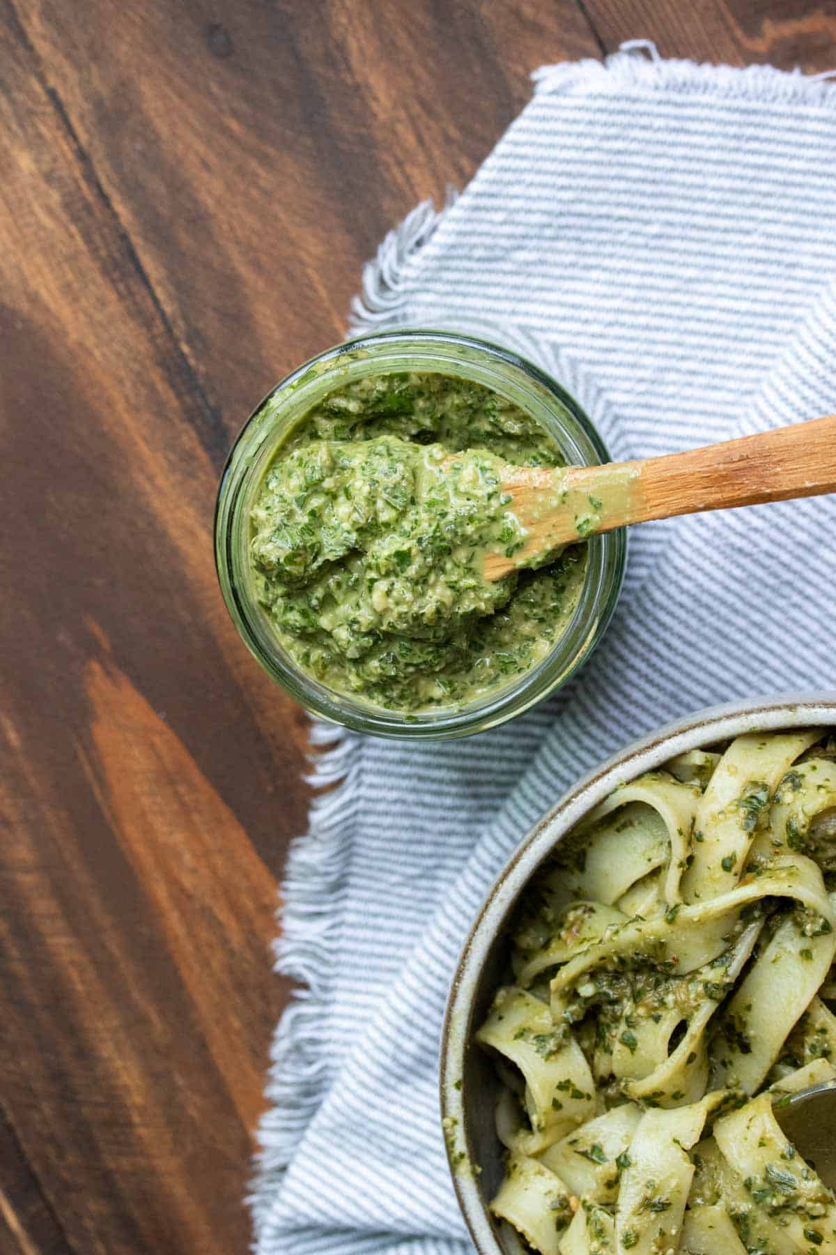 Wooden spoon getting a scoop of pesto from a glass jar