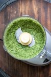 Top view of a food processor with blended pesto inside sitting on a wooden surface