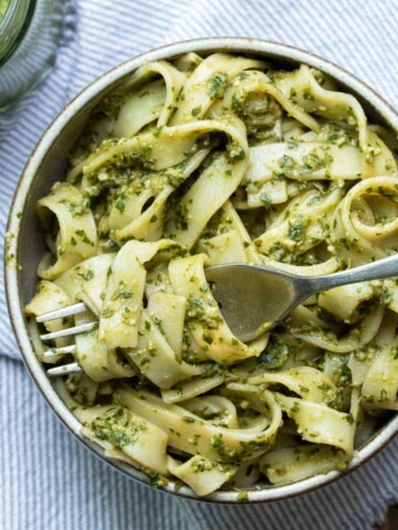 Fork with flat pesto pasta wound around it sitting on a grey bowl