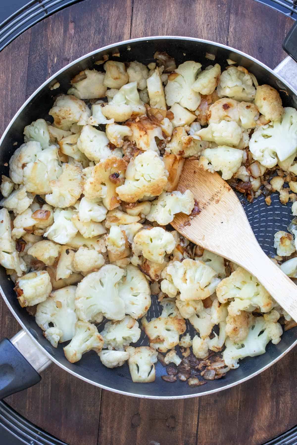 Wooden spoon mixing cauliflower in a saute pan