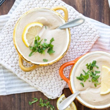 Two soup bowls with pureed cauliflower soup topped with parsley and lemon