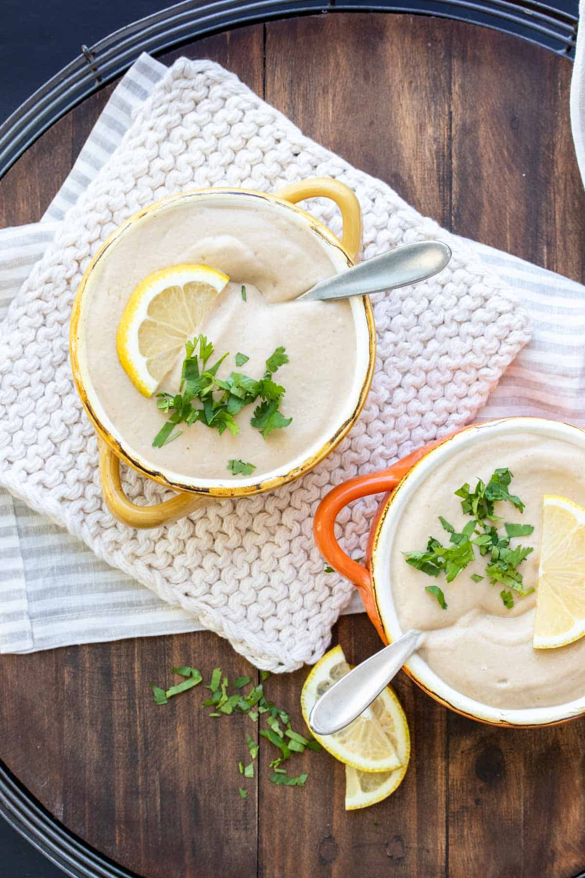 Two soup bowls with pureed cauliflower soup topped with parsley and lemon