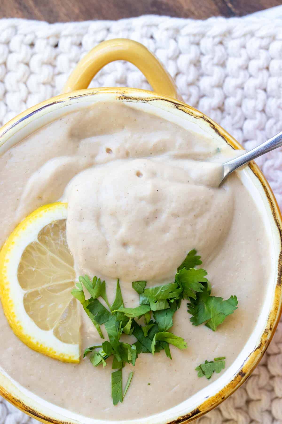 Spoon getting a bite of cauliflower soup from a yellow soup bowl