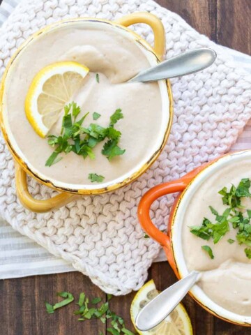 Yellow and orange soup bowls filled with cauliflower soup and sprinkled with chopped parsley