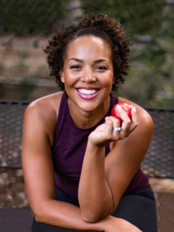 A black woman sitting holding an apple with her elbow on her other arm