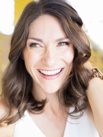 A woman wearing a white tank top smiling and pushing back her hair