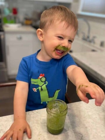 Photo of a boy pointing with green smoothie on his lip laughing and pointing