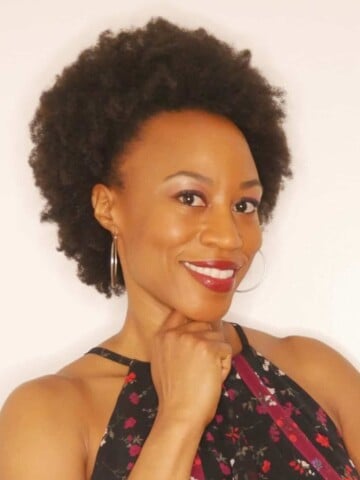 A black woman with short hair smiling with her hand under her chin